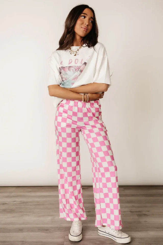 Woman wearing pink and white checkerboard wide leg pants with a graphic t-shirt and white sneakers.