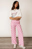 Woman wearing pink and white checkerboard wide leg pants with a graphic t-shirt and white sneakers.