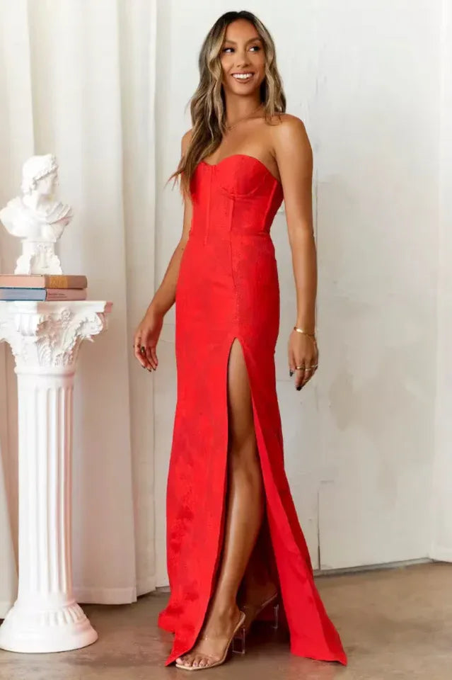 Full view of a woman in a red formal dress with a thigh-high slit showcasing her leg.