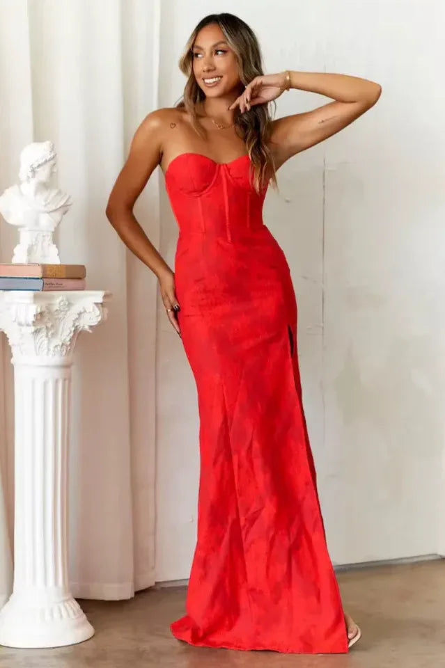 Model posing in a red strapless maxi dress with a side slit.