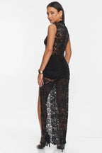 Woman wearing a black lace maxi dress with a high neckline and a thigh-high slit, back view.
