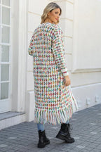 Rear view of a woman wearing a long, multi-colored tweed-inspired knit cardigan with fringe detail, blue jeans, and black boots.