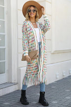 Woman in a tan fedora hat, sunglasses, and a long, multi-colored tweed-inspired knit cardigan with fringe detail, holding a clutch.