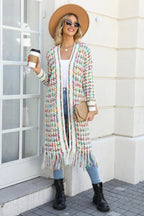 Woman in a tan fedora hat, sunglasses, and a long, multi-colored tweed-inspired knit cardigan with fringe detail, holding a coffee cup and a clutch.