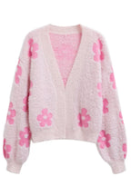 A pink fluffy knit cropped cardigan with a floral print, laid flat.