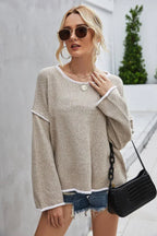 Woman wearing a beige textured knit sweater with white trim and denim shorts, holding a black handbag.