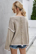 Back view of a woman wearing a beige textured knit sweater with white trim and denim shorts, showing fringe detail on the back.