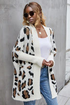 Woman wearing a white leopard print long cardigan over a white tank top and blue jeans.