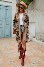Woman wearing a tan geometric print long cardigan, white t-shirt, denim shorts, brown cowboy boots, and a wide-brimmed hat, standing outdoors