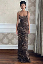 Woman wearing a long leopard print slip dress with spaghetti straps, standing indoors.