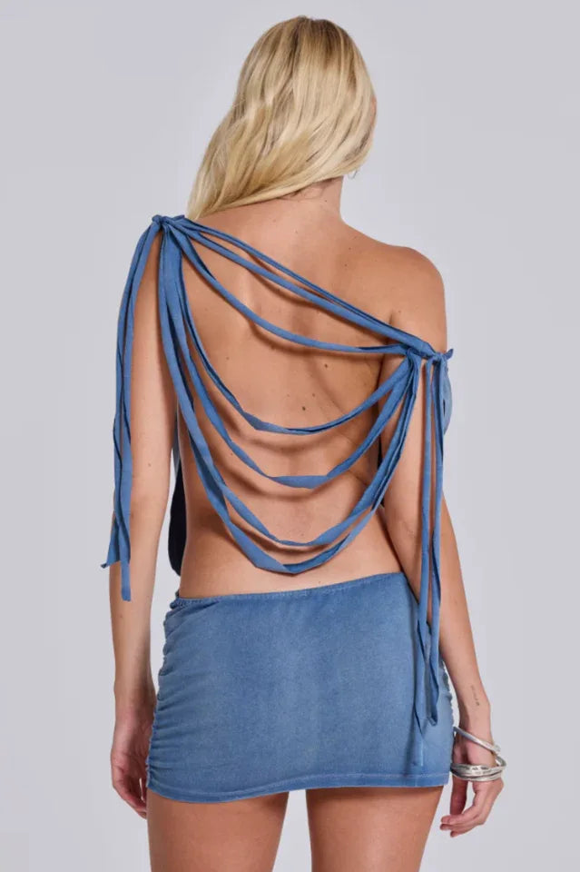 Back view of a woman in a distressed denim dress, highlighting the strappy back.