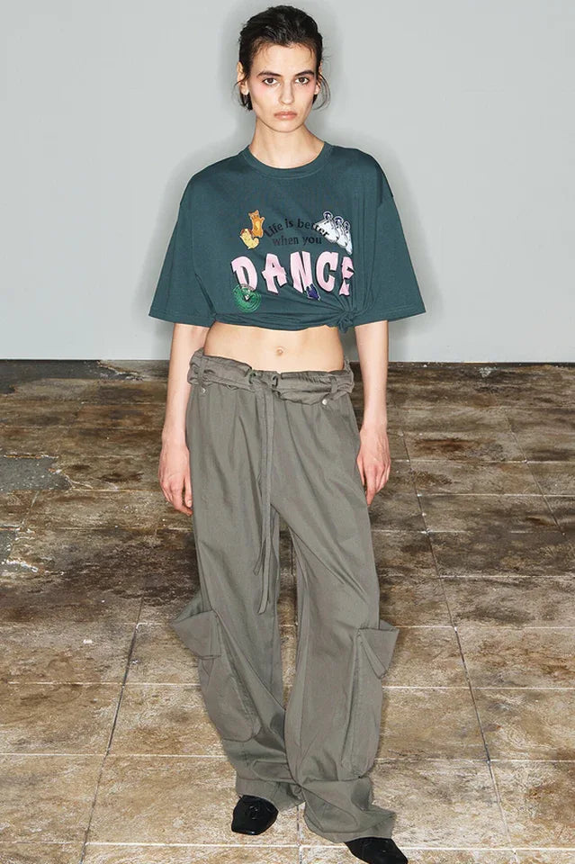 Model wearing a dark green cropped t-shirt with a graphic print and wide-leg olive green cargo pants.