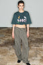 Model wearing a dark green cropped t-shirt with a graphic print and wide-leg olive green cargo pants.