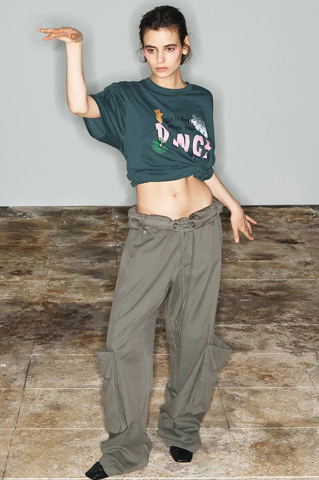 Model in a dark green cropped t-shirt with a graphic print and wide-leg olive green cargo pants, striking a pose. Secondary image