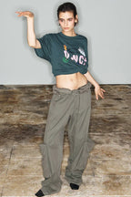 Model in a dark green cropped t-shirt with a graphic print and wide-leg olive green cargo pants, striking a pose.