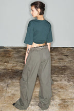 Rear view of a model wearing a dark green cropped t-shirt with a graphic print and wide-leg olive green cargo pants.