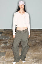 Model wearing a distressed cream-colored cropped sweater and wide-leg olive green cargo pants, with a pink baseball cap.