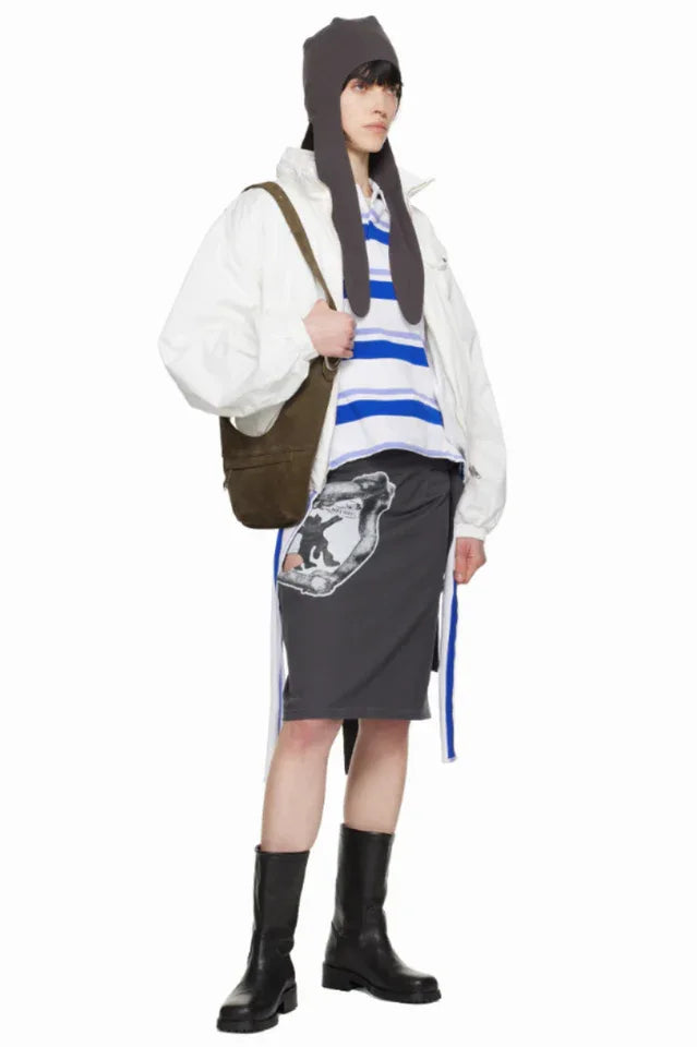 Model wearing a grey graphic print midi skirt with cut-out details and a tie detail, paired with a white jacket, striped top, and black boots. Main image