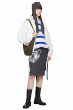 Model wearing a grey graphic print midi skirt with cut-out details and a tie detail, paired with a white jacket, striped top, and black boots.
