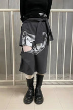 Model wearing a grey graphic print midi skirt with cut-out details and a tie detail, styled with a black top, white socks, and platform boots.