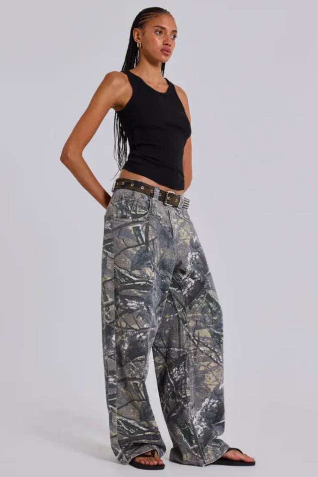 Woman wearing a black tank top and camouflage wide-leg jeans, standing from the side.
