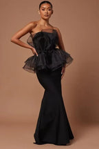Woman wearing a black strapless formal gown with a ruffled peplum bodice and mermaid skirt.