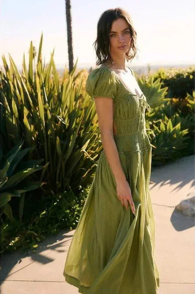 Side view of a woman in a green puff-sleeve midi dress with a smocked bodice and flowing skirt, outdoors.