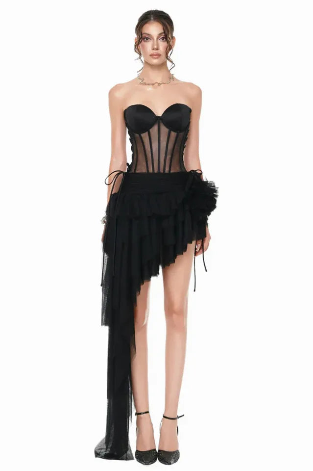 Woman wearing a black strapless corset dress with an asymmetrical ruffled skirt and long tulle train, front view. Main image