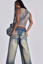 Model wearing wide leg jeans with a grey tank top and a denim bag, side back view showing graphic detail.