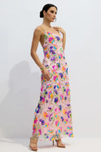 Woman wearing a pink floor-length gown with colorful floral sequins and gold chain straps, standing against a white background.