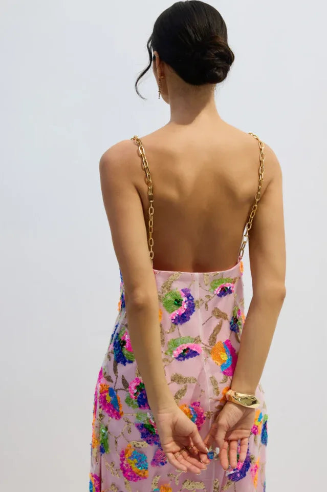 Back view of a woman in a pink sequined floral gown with gold chain straps, showing the open back.