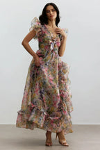Woman standing in a floral print chiffon gown with V-neck, bow detail, flutter sleeves, and a high-low hemline.