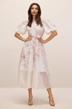 Woman wearing a floral print midi dress with puff sleeves and a tie waist.