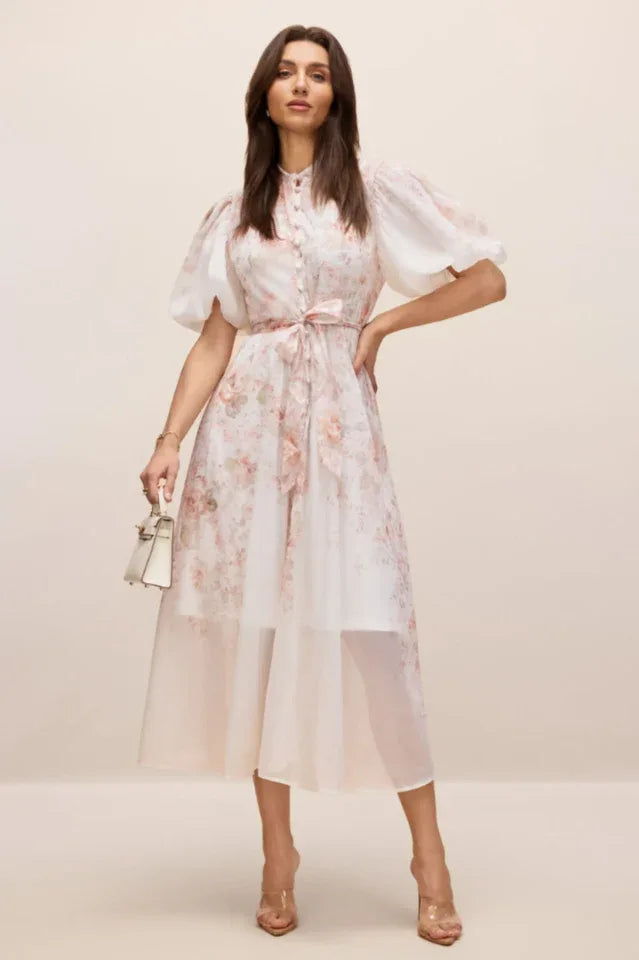 Woman in a floral dress holding a white handbag. Secondary image