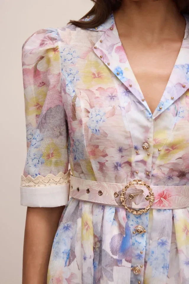 Close-up of the bodice of a floral print dress, showing the collar, buttons, belt, and puff sleeve detail