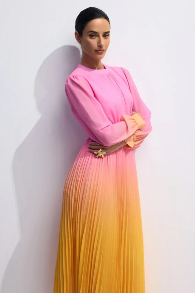 Close-up of a model's upper body in a pink to yellow ombre pleated chiffon maxi dress, showing the gathered neckline and a statement ring.
