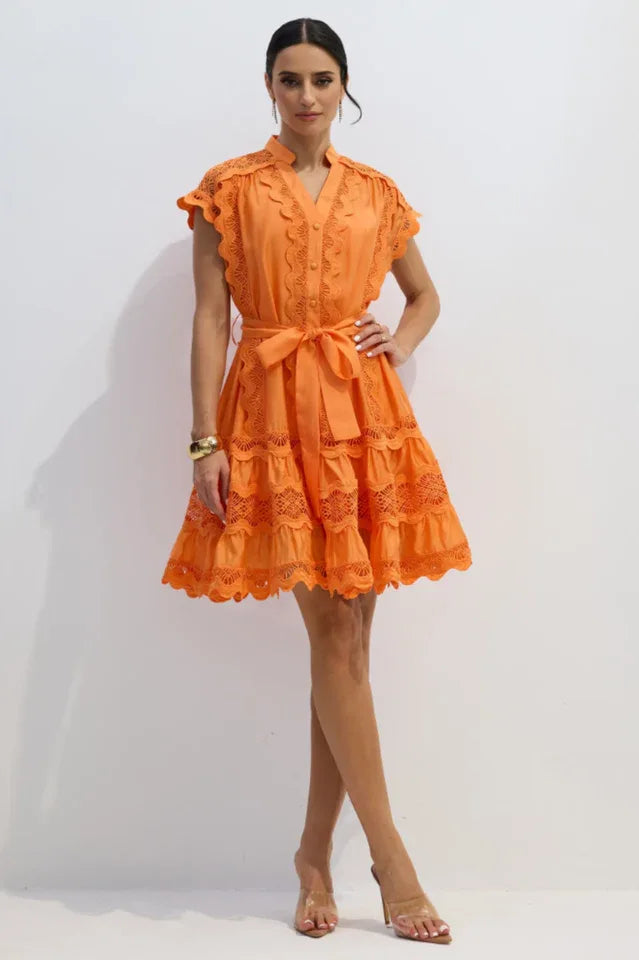 Woman wearing an orange lace dress with a tie waist and a gold bracelet.