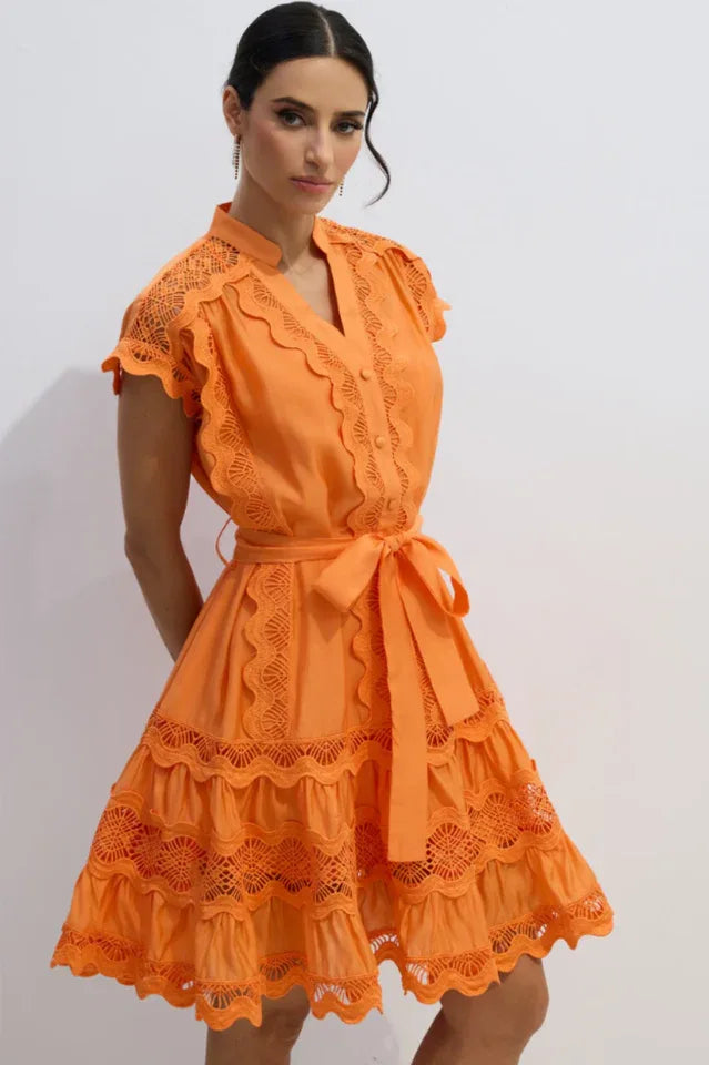 Woman posing with her hands behind her back in an orange lace dress.