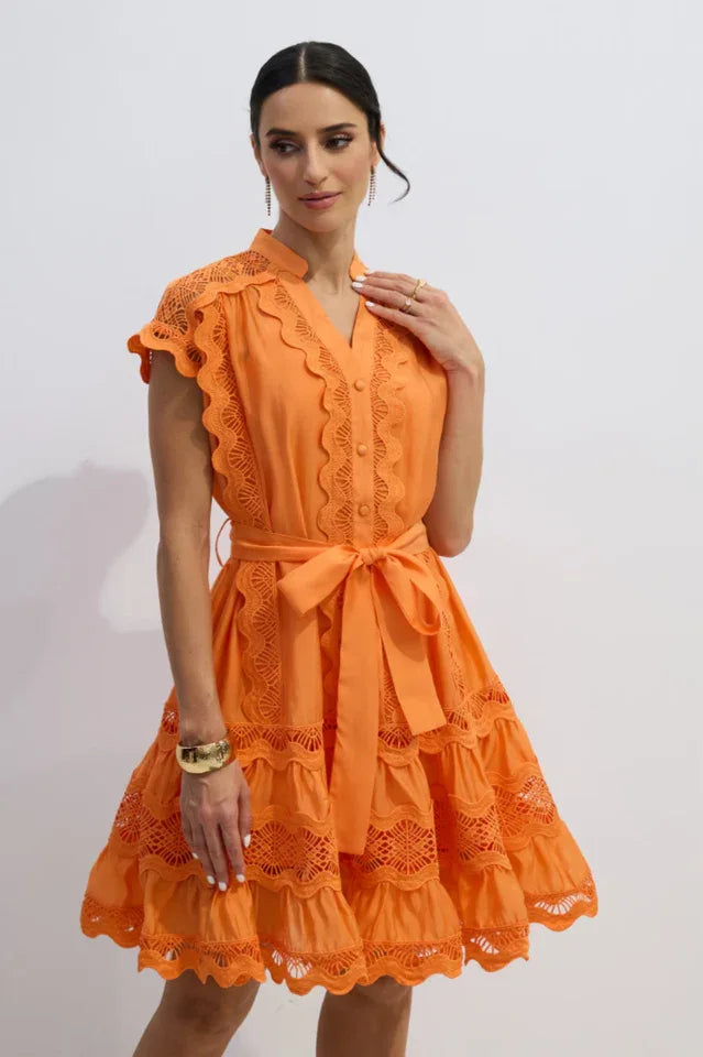 Full body shot of a woman in an orange lace dress with a tie waist.