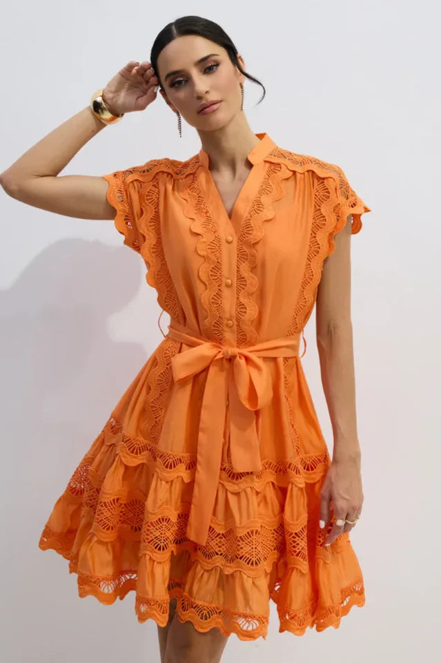 Woman wearing an orange lace-trimmed dress with a tie waist.