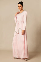 Woman posing in a light pink, long-sleeved formal dress with a pleated skirt and embellished details.