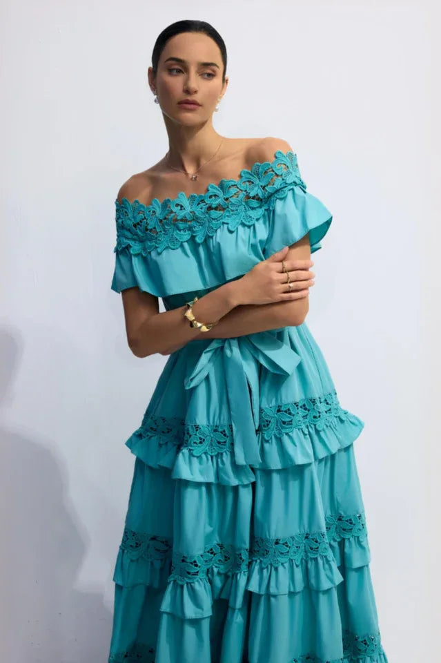 Close-up of a woman in a turquoise off-the-shoulder maxi dress, showing the lace neckline and ruffled tiers.