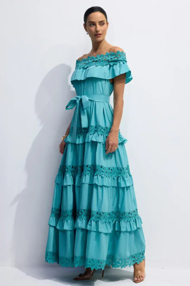 Side view of a woman wearing a turquoise ruffled maxi dress with off-the-shoulder neckline and lace trim.