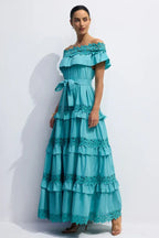 Side view of a woman wearing a turquoise ruffled maxi dress with off-the-shoulder neckline and lace trim.