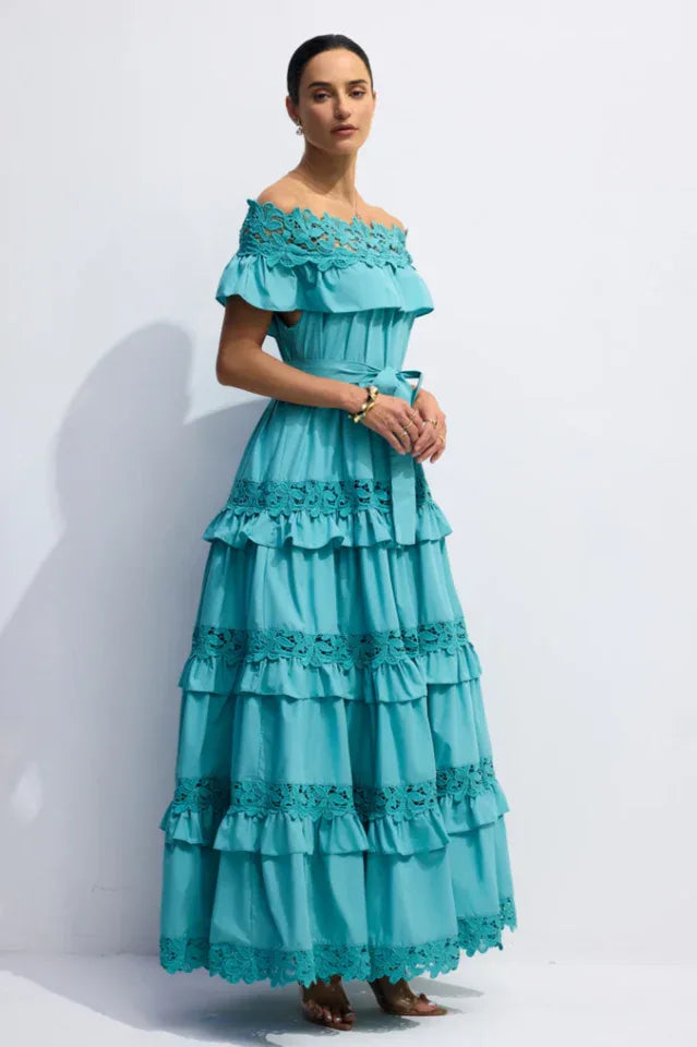 Model posing in a turquoise off-the-shoulder tiered maxi dress with lace detailing.