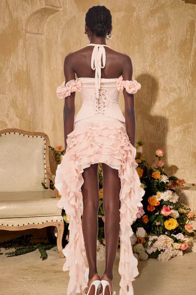 Back view of a model wearing a pink ruffled corset dress with a halter neckline and high-low hemline.