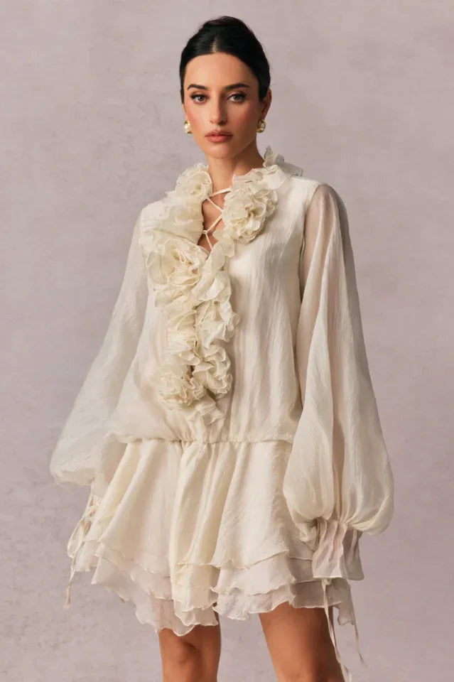 woman wearing a white sheer chiffon mini dress with a ruffled neckline and floral embellishments
