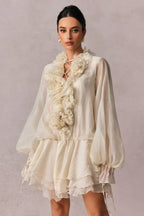 woman wearing a white sheer chiffon mini dress with a ruffled neckline and floral embellishments