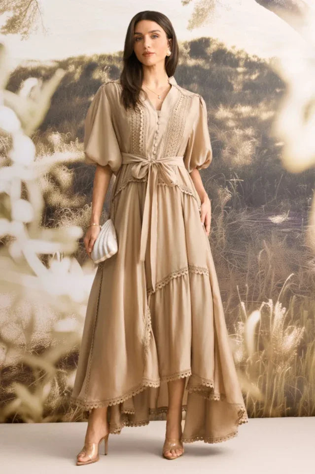 Woman wearing a tan linen blend maxi dress with puffed sleeves and a tiered skirt, holding a shell-shaped clutch. Secondary image