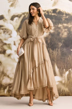 Woman wearing a tan linen blend maxi dress with puffed sleeves and a tiered skirt, adjusting her earring.